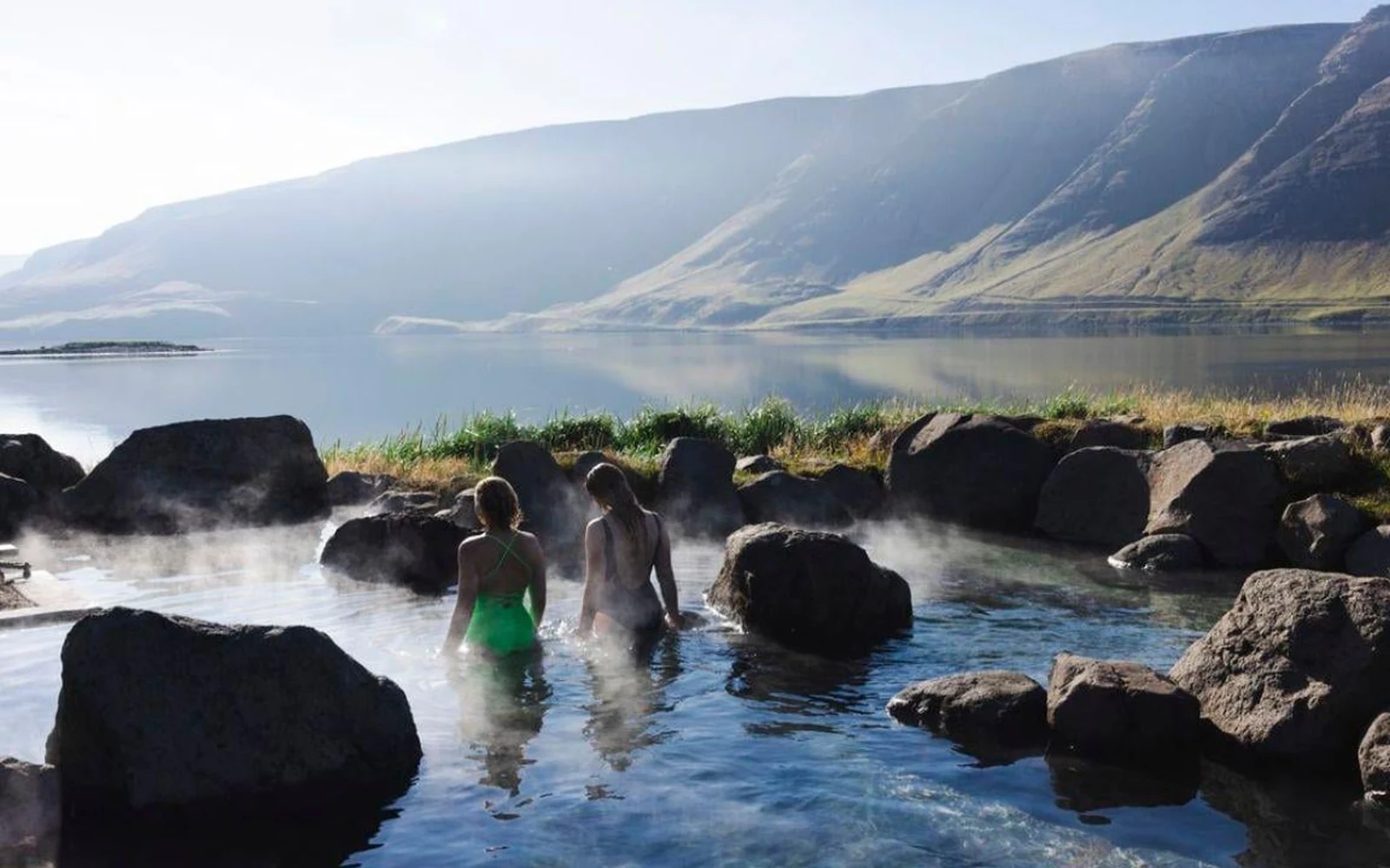Dampf steigt von einem warmen Fluss auf, der durch ein grünes Geothermal-Tal in Island fließt