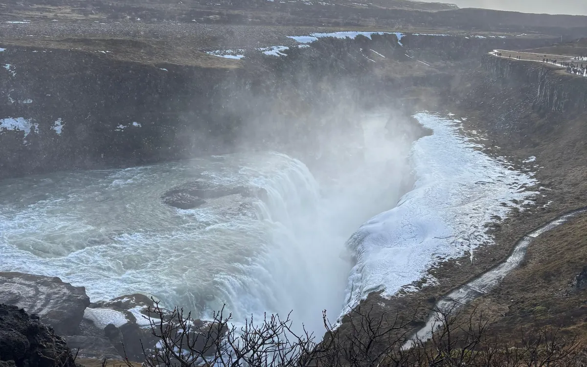 Ein flacher, dampfender Fluss durch ein grünes Tal, in dem Menschen im warmen Wasser sitzen